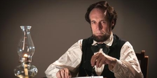 Dennis Boggs as Abraham Lincoln sits at a desk.