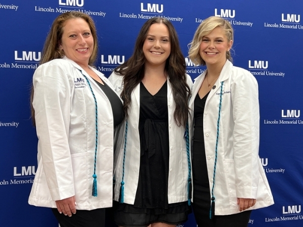 Three students with white coats and cords.