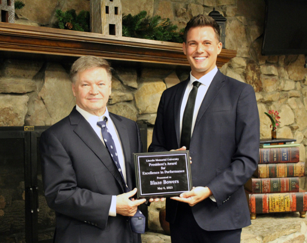 LMU President Clayton Hess presents Assistant Vice President for Academic and Support Services Blaze Bowers with the President's Award and they hold a plaque between them.