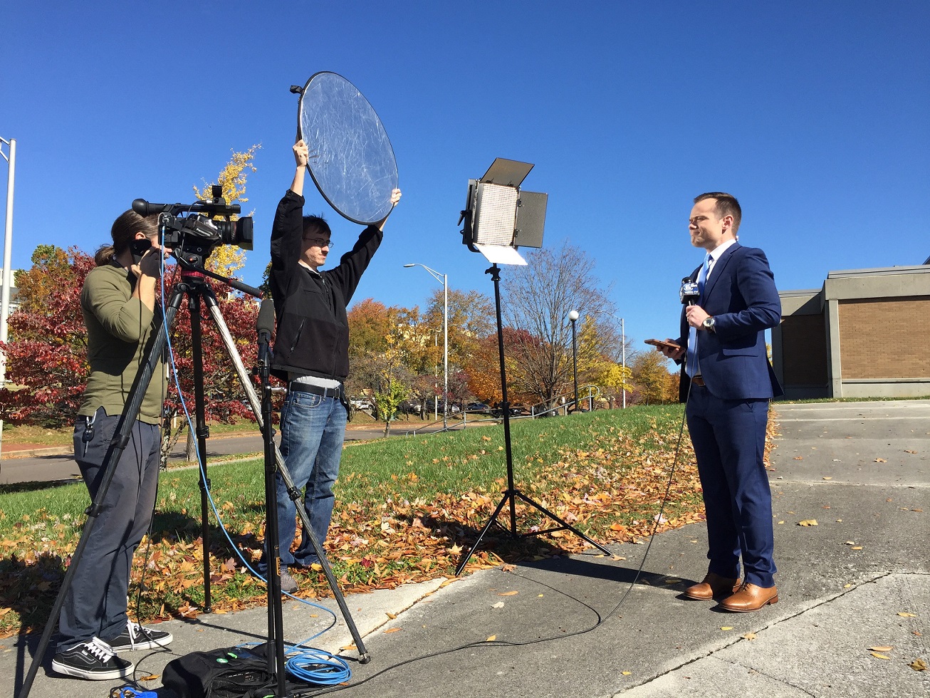 LMU student holds light reflector for live news.