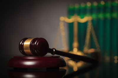 Gavel in foreground, blurred scales of justice and books in background.