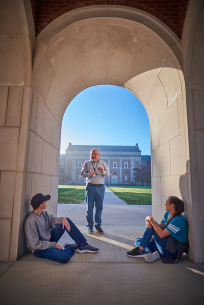 Two students sitting, instructor standing on LMU quad.