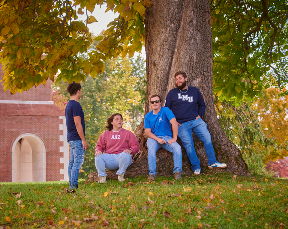 A picture of four students sitting next to a tree on campus.