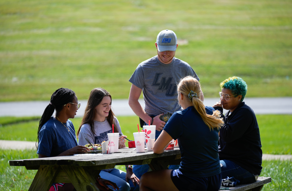 A group of students having lunch at a picnic table. 