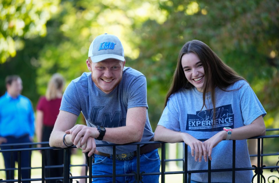 Two students leaning against a rail on campus.