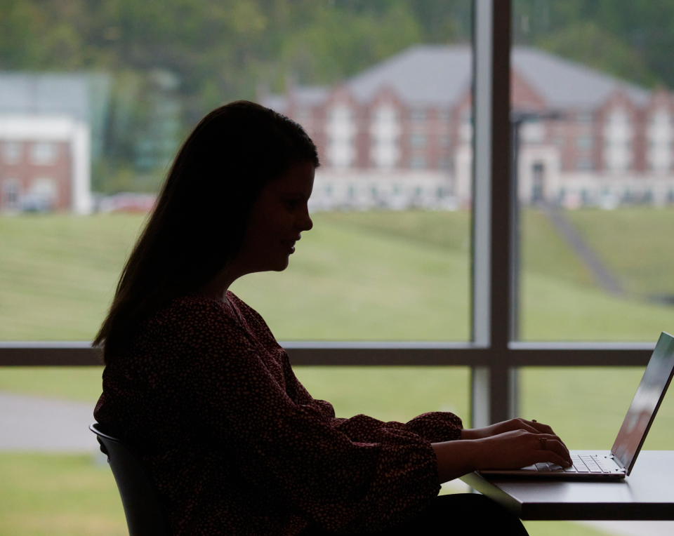 Student working on her laptop in front of a window.