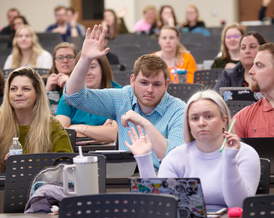 Students in a classroom with their hands raised.